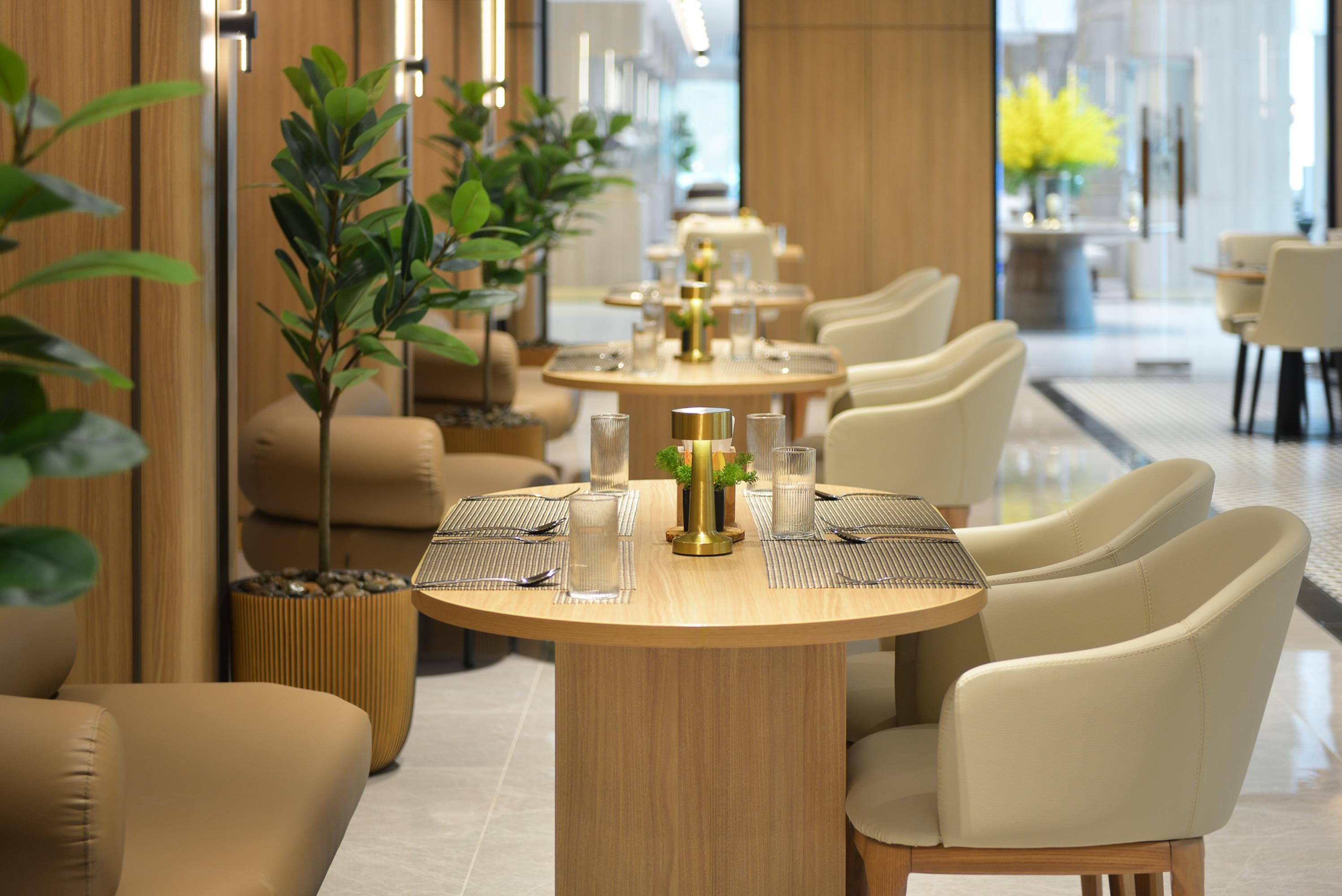 Een stijlvolle eetruimte met ronde tafels, beige stoelen en potplanten.