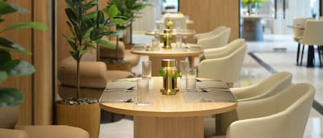 A modern dining area with round tables, beige chairs, and potted plants.