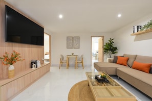 A modern living room with a flat-screen TV, a sofa, a coffee table, and a dining area with chairs.