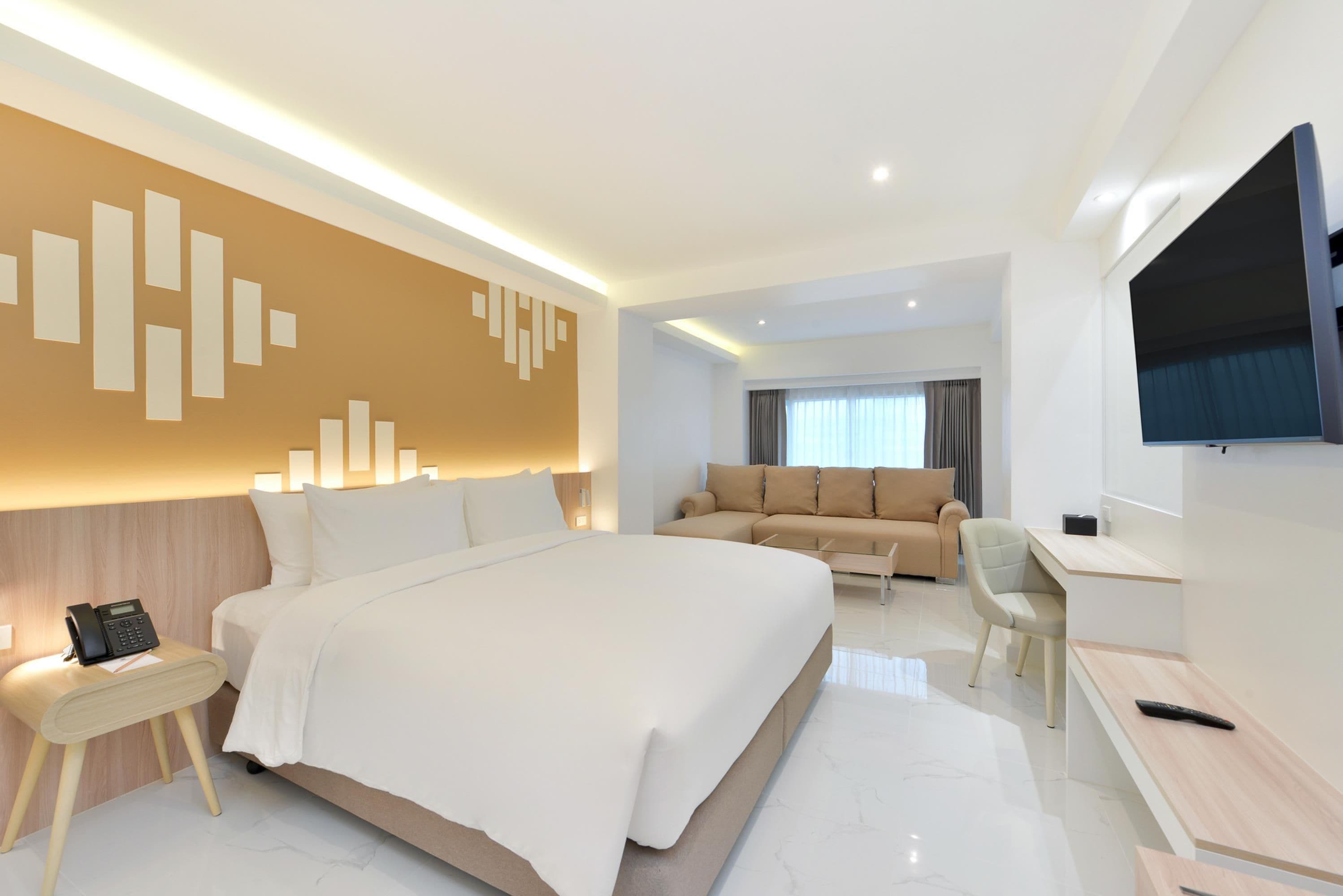A modern hotel room with a large bed, a sofa, a desk, and a TV.