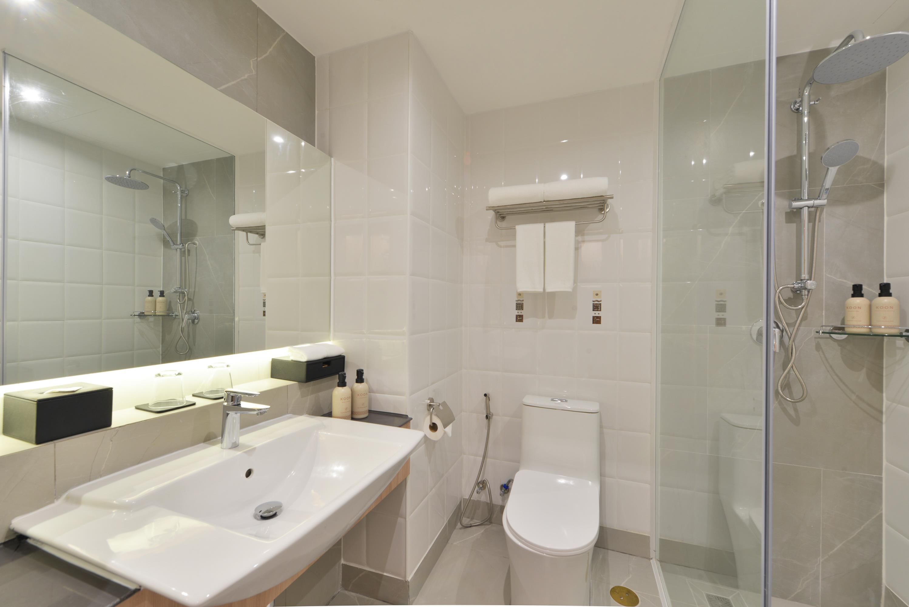 A modern bathroom with a large mirror, a sink, a toilet, and a shower area.