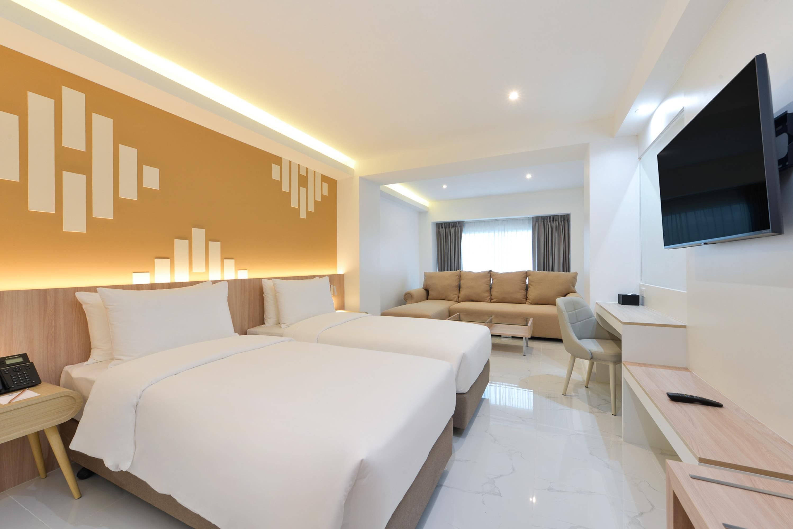 A hotel room with two beds, a sofa, a desk, and a TV.