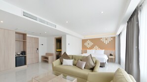 Una habitación de hotel moderna con sofá, una mesa de centro de vidrio, cama y baño visible a través de una puerta abierta.