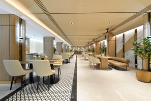 A modern hotel lobby with a central walkway, seating areas, and a staircase.