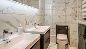 A modern bathroom with marble walls, a dual sink vanity, a toilet, and a built-in mirror. - 4 Bed in Norwich (oc-90094) (Stratton Strawless)