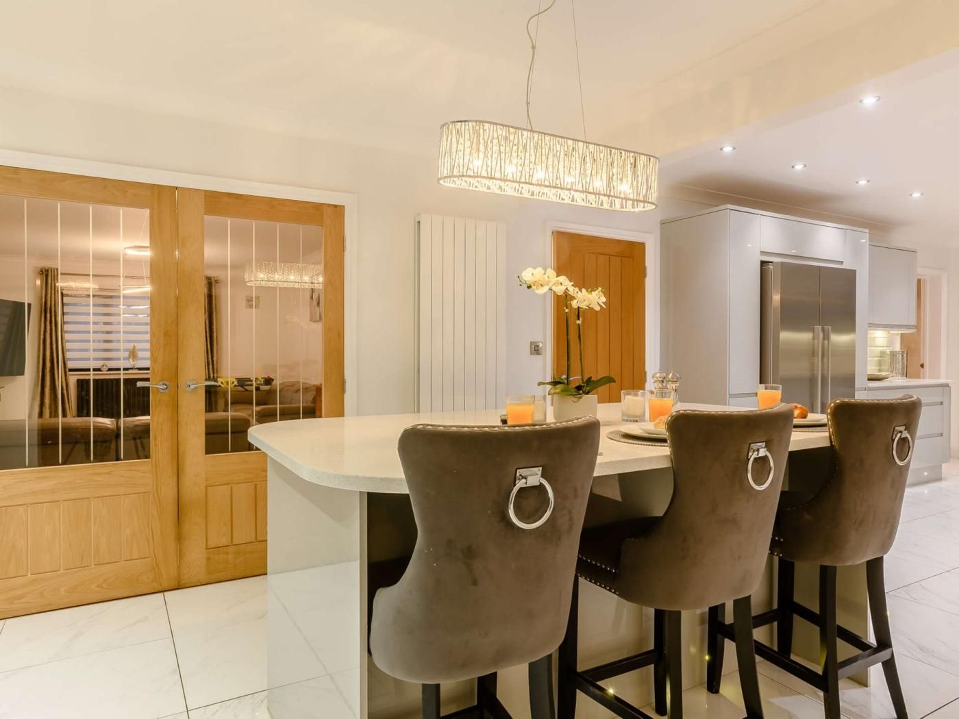 A modern kitchen with a central island, bar stools, a refrigerator, and a dining area with a table and chairs.