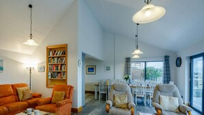 A spacious living area with a sofa, armchairs, a coffee table, a bookshelf, and a dining area with chairs and a table. - 5 Bed in Aberdovey (oc-90222) (Aberdovey)