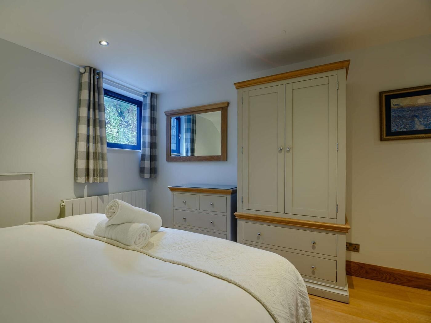 Quarto com cama, guarda-roupa, radiador, janela com cortinas e espelho.