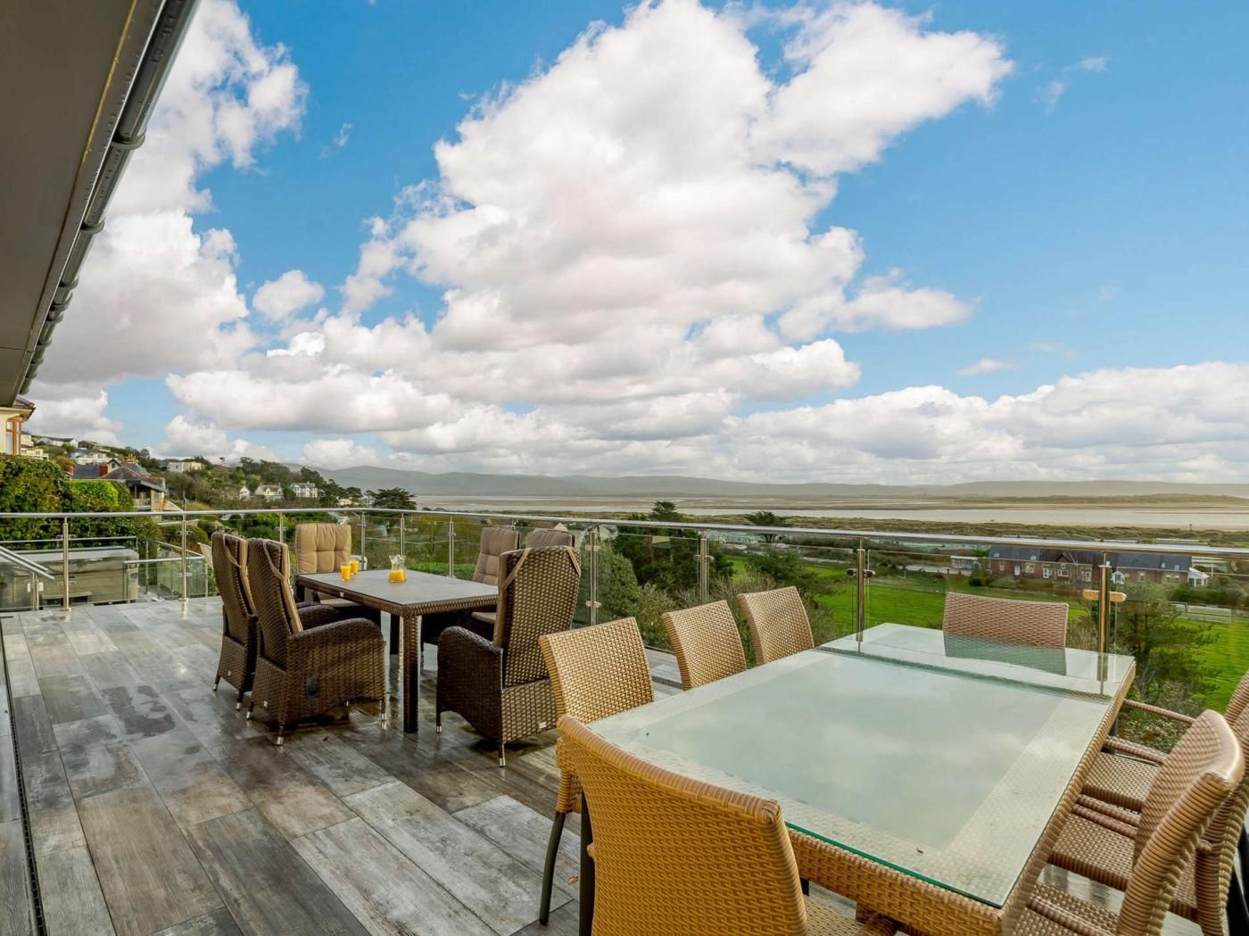 Un balcon doté de meubles en osier et d’une table en verre, offrant une vue sur un paysage côtier.