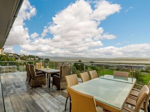 A balcony with wicker furniture and a glass table, overlooking a coastal landscape. - 5 Bed in Aberdovey (oc-90222) (Aberdovey)