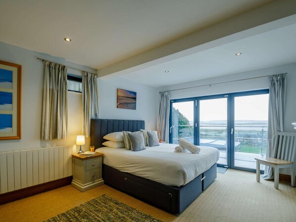 Une chambre à coucher avec un lit, une table de chevet, une lampe et une vue sur l’extérieur grâce à une grande fenêtre.