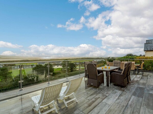 A terrace with wicker furniture and a glass balustrade overlooking a landscape. - 5 Bed in Aberdovey (oc-90222) (Aberdovey)
