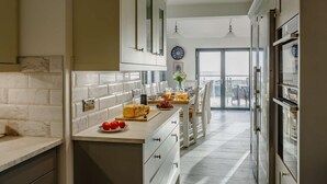 A modern kitchen with marble backsplash, white cabinetry, and a dining area with a view. - 5 Bed in Aberdovey (oc-90222) (Aberdovey)