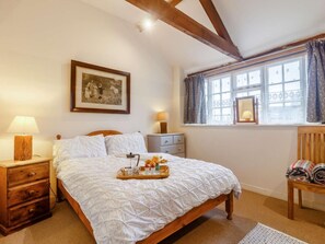 Une chambre à coucher avec un lit en bois, une table de chevet avec une lampe, une commode, une fenêtre avec des rideaux et un tableau encadré accroché au mur.