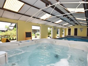 Una piscina interior con hidromasaje, ventanas amplias y un cartel visible de advertencia sobre la profundidad.