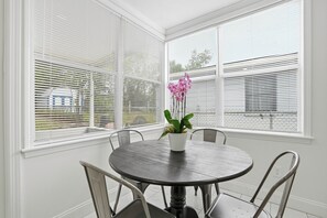 A round dining table with four chairs, a potted plant with pink flowers, and white blinds on the windows. - Spacious and comfortable house in Avondale. Ideal for longer stays. Pet friendly (Jacksonville)