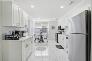 A modern kitchen with white cabinetry, a stainless steel refrigerator, a dining table with chairs, and a window with blinds. - Spacious and comfortable house in Avondale. Ideal for longer stays. Pet friendly (Jacksonville)