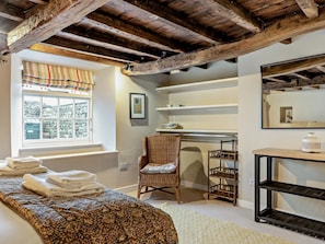 Ein Zimmer mit einem Bett, einem Sessel, einem Regal und einem Fenster mit Blick auf eine Steinmauer.