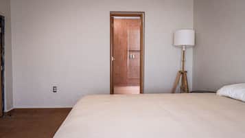 A hotel room with a bed, a wooden door, a floor lamp, and a wall socket.
