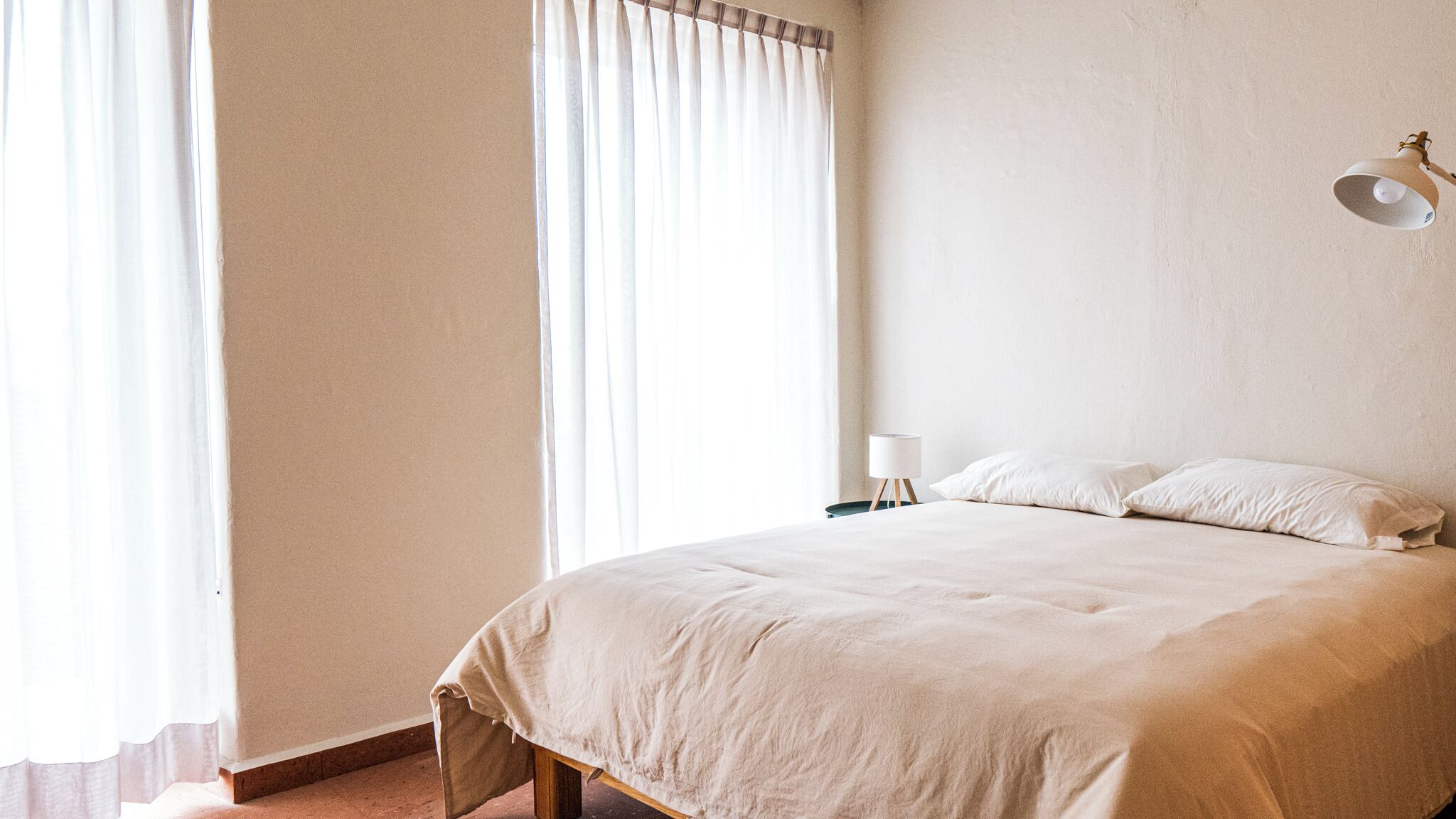 Quarto com cama, cortinas, abajur e luminária na parede.