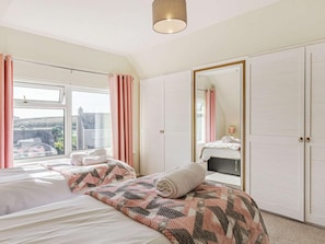 A bedroom with a large bed, a wardrobe, a mirror, and a window with curtains. - 3 Bed in Bude (oc-89425) (Bude)