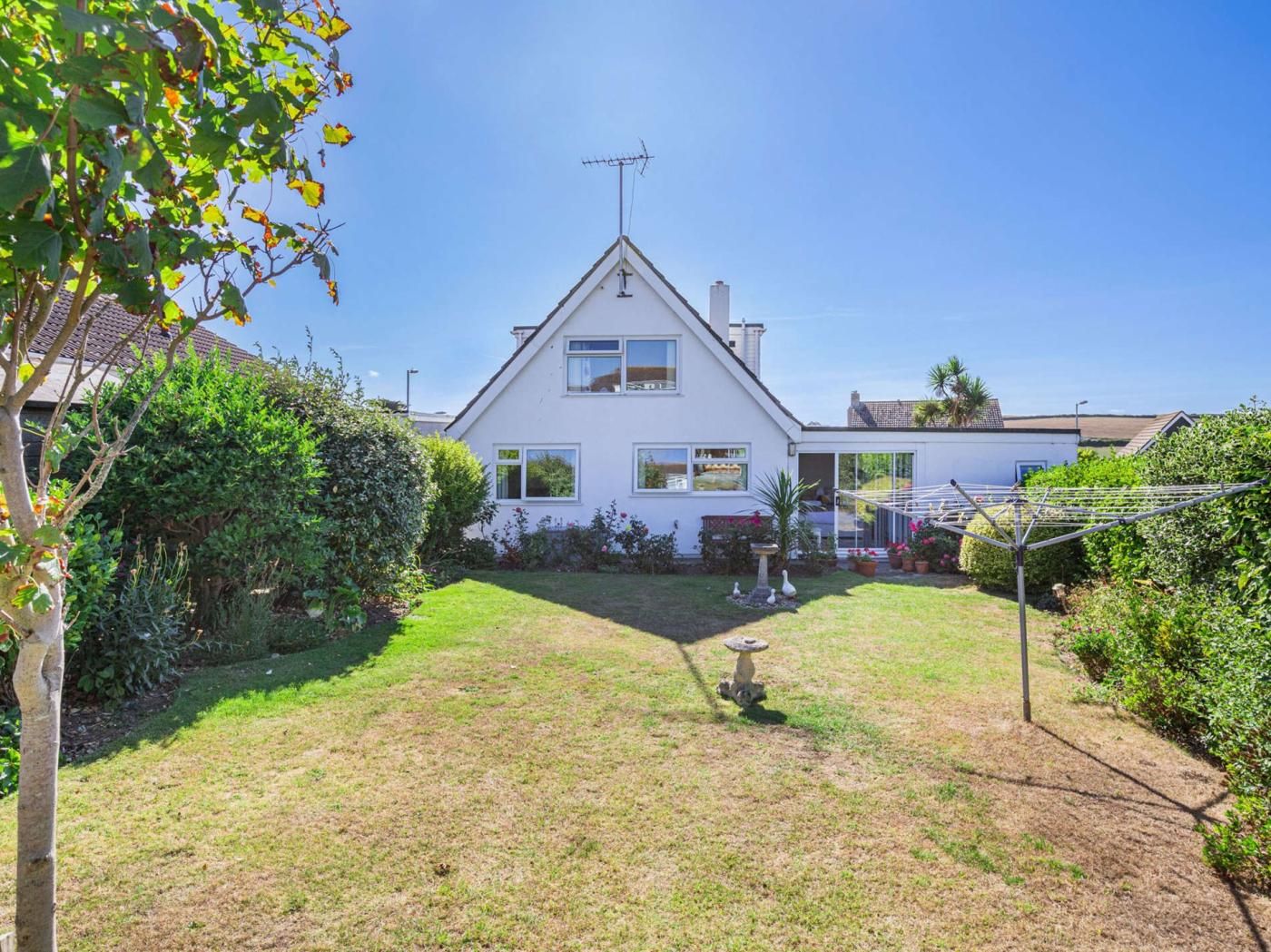 Ein eingeschossiges Haus mit geneigtem Dach, einem sichtbaren Schornstein und einem kleinen Garten mit Rasenfläche und verschiedenen Pflanzen.