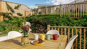 A wooden deck with a table set for two, a vase of flowers, and a stone wall in the background. - 2 Bed in Ilfracombe (oc-89570) (Combe Martin)