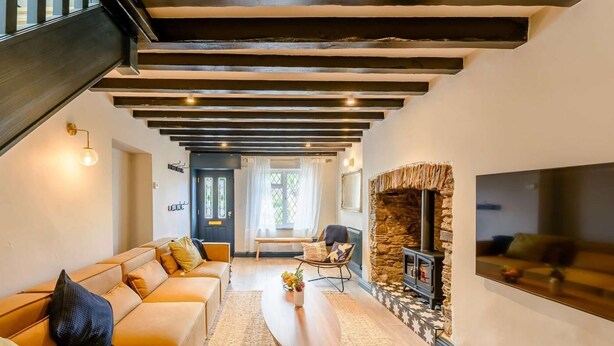 A modern living room with a sofa, a coffee table, a stone fireplace, and a TV mounted on the wall. - 2 Bed in Ilfracombe (oc-89570) (Combe Martin)
