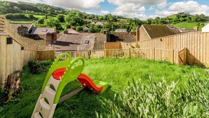 A rural village with houses, a wooden fence, and a green slide in a grassy area. - 2 Bed in Ilfracombe (oc-89570) (Combe Martin)