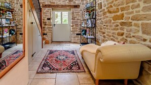 Habitación con paredes de piedra, un sofá, una alfombra estampada y una puerta que da a otra zona.