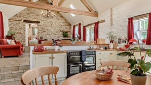 Una cocina rústica con paredes de piedra, vigas de madera y un comedor con una mesa redonda y sillas.