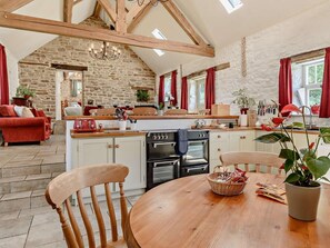 A rustic kitchen with stone walls, wooden beams, and a dining area with a round table and chairs. - 2 Bed in Matlock (oc-89985) (Lea)