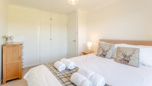 Een slaapkamer met een bed, twee kussens met hertenprint, een bedlampje, een houten kast en een hanglamp.