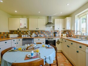 A kitchen with a dining table set for breakfast, a dishwasher, an oven, and a window with a view. - 3 Bed in Hunstanton (oc-90011) (Sedgeford)
