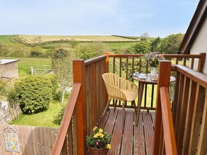 Eine Holzterrasse mit Stuhl und Tisch, umgeben von Grünpflanzen und Feldern.