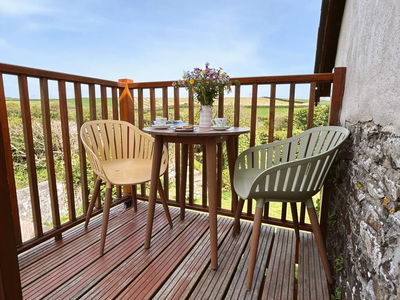 Una terraza de madera con dos sillas y una mesa, con vistas a un paisaje verde.