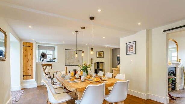 A dining area with a wooden table, white chairs, and hanging pendant lights. - 5 Bed in Crickhowell (oc-90053) (Glangrwyney)