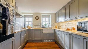 A modern kitchen with grey cabinets, a wooden countertop, a built-in oven, and a clock on the wall. - 5 Bed in Crickhowell (oc-90053) (Glangrwyney)
