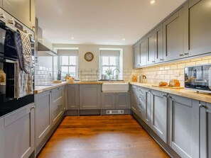 A modern kitchen with grey cabinets, a wooden countertop, a built-in oven, and a clock on the wall. - 5 Bed in Crickhowell (oc-90053) (Glangrwyney)
