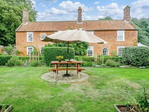 A brick house with a garden patio featuring a wooden table and a large umbrella. - 5 Bed in Dereham (oc-89542) (Swanton Morley)