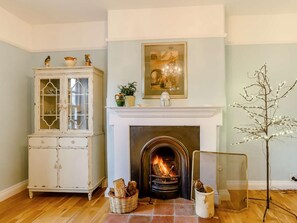 A room with a fireplace, a cabinet with glass doors, a framed picture above the mantel, and a tree with lights. - 5 Bed in Dereham (oc-89542) (Swanton Morley)