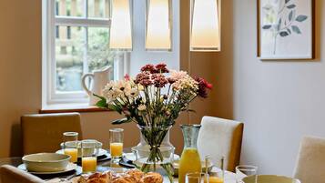 A dining table set with plates, glasses, and a vase of flowers, with a window and artwork in the background.