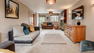 A modern living room with a sofa, a coffee table, and a rug. There is a wooden cabinet and a television on the wall.