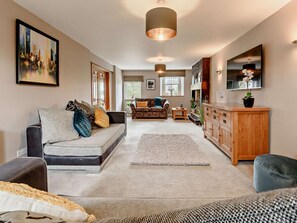 Ein modernes Wohnzimmer mit einer Couch, einem Couchtisch und einem Teppich. Es gibt eine Holzkommode und ein Fernsehgerät an der Wand.