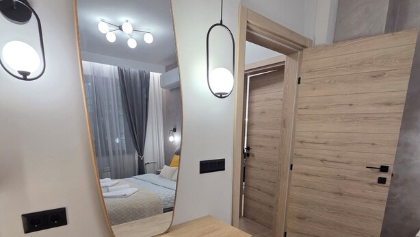 Quarto moderno com um espelho grande, luminárias de cabeceira, um guarda-roupa de madeira e um pequeno banquinho.
