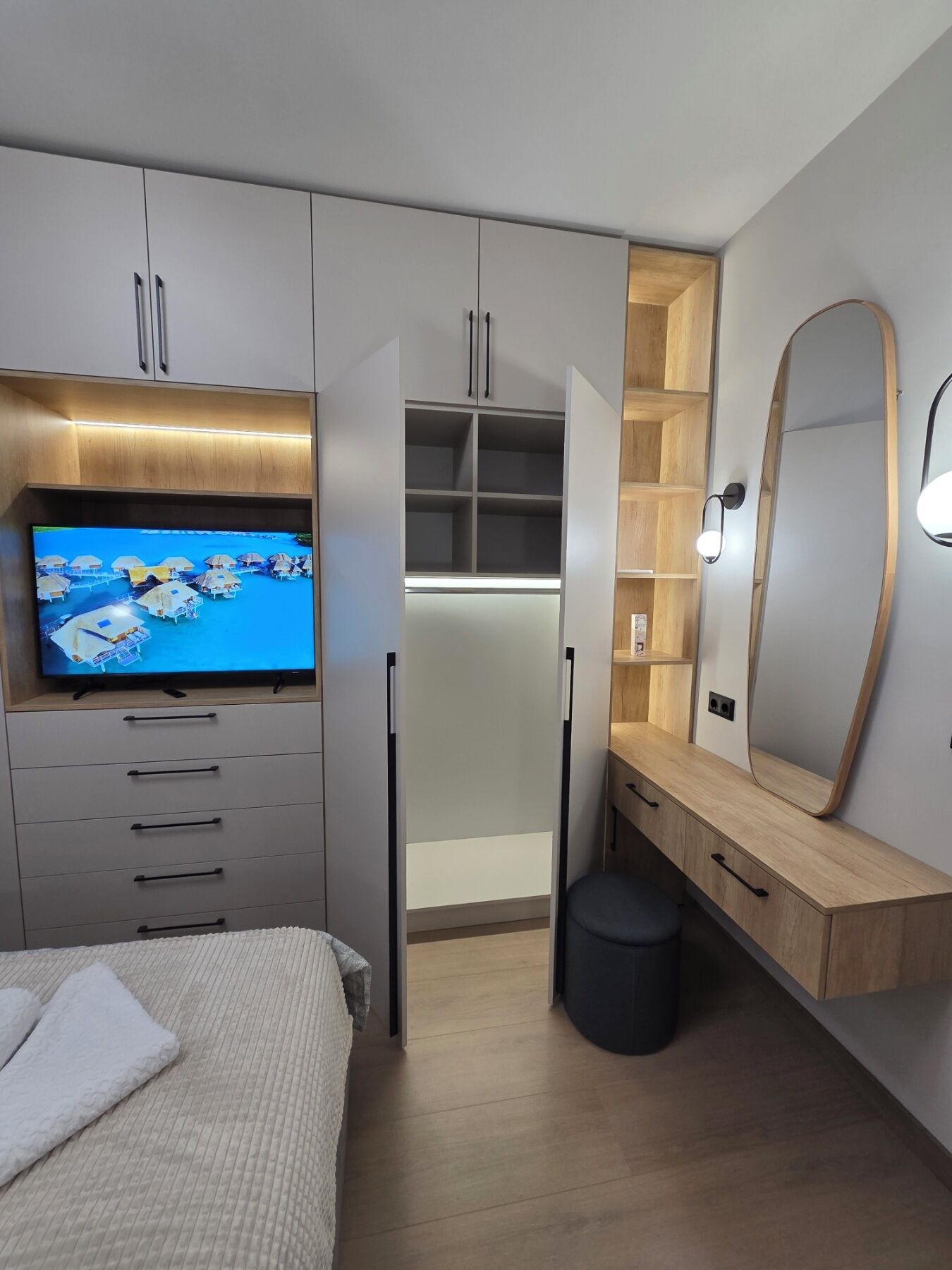 Une chambre avec une télévision, une armoire, une coiffeuse et un petit tabouret.