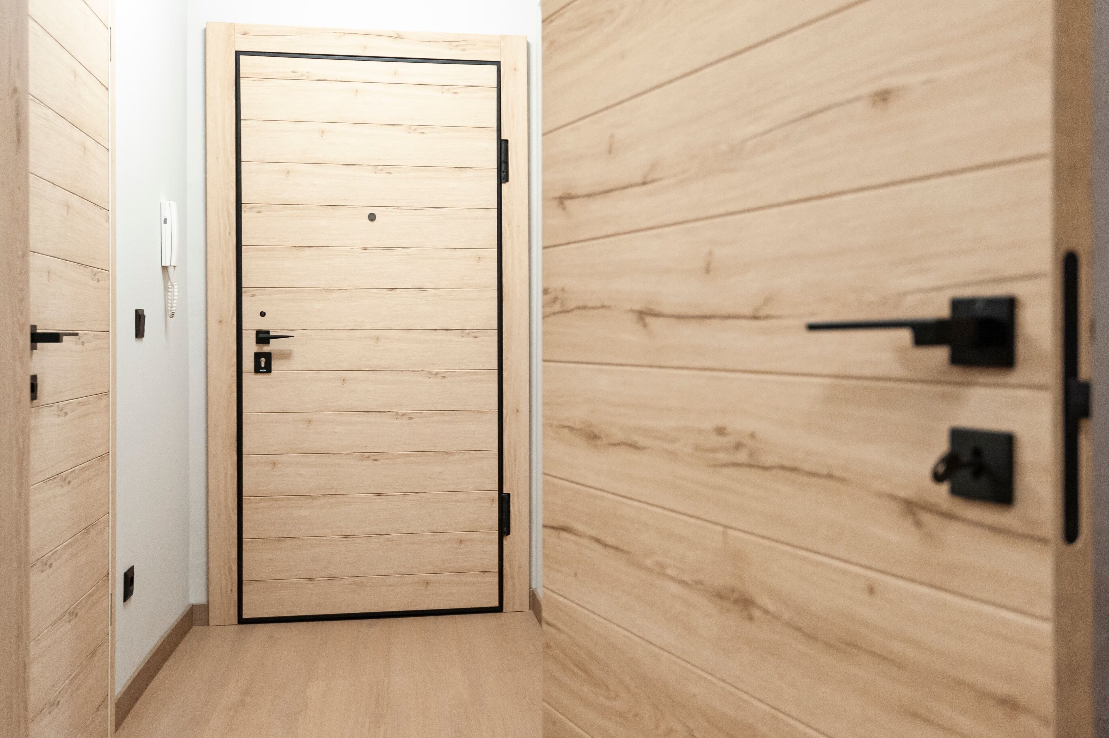 A hallway with a wooden door, a light switch, and a thermostat on the wall.