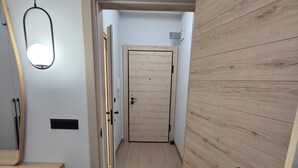 Um corredor com porta de madeira, luminária e espelho.
