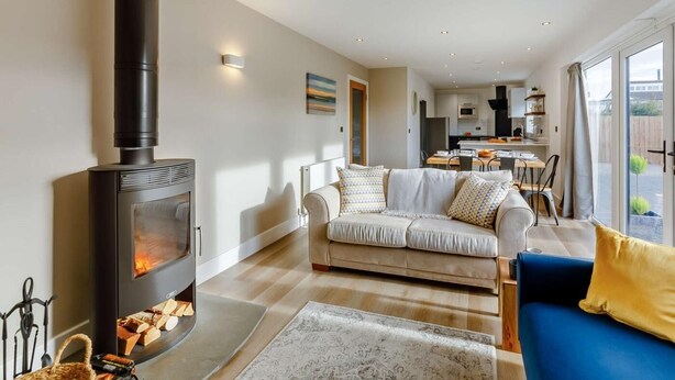 Una sala de estar con chimenea, un sofá, un sillón azul y una zona de comedor al fondo.