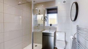 Un baño moderno con cabina de ducha de vidrio, lavamanos, inodoro y espejo.